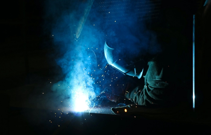 Person welding in dark room to represent manufacturing and production in the product design services stage