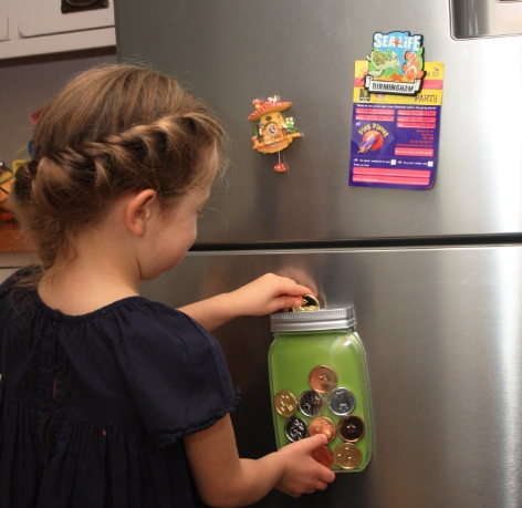 Child putting token into reward jar on fridge